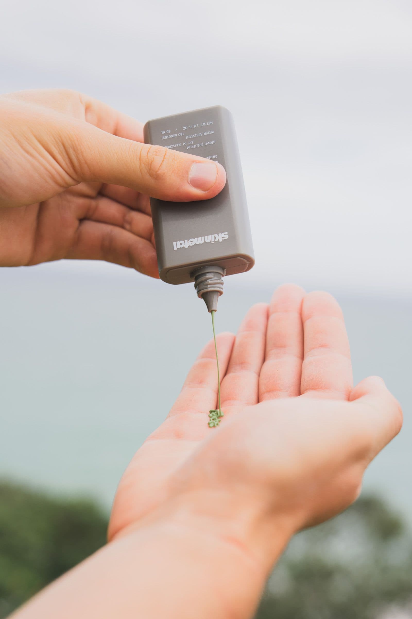 A small dollop of green sunscreen rests in the center of an open palm held out over the ocean.