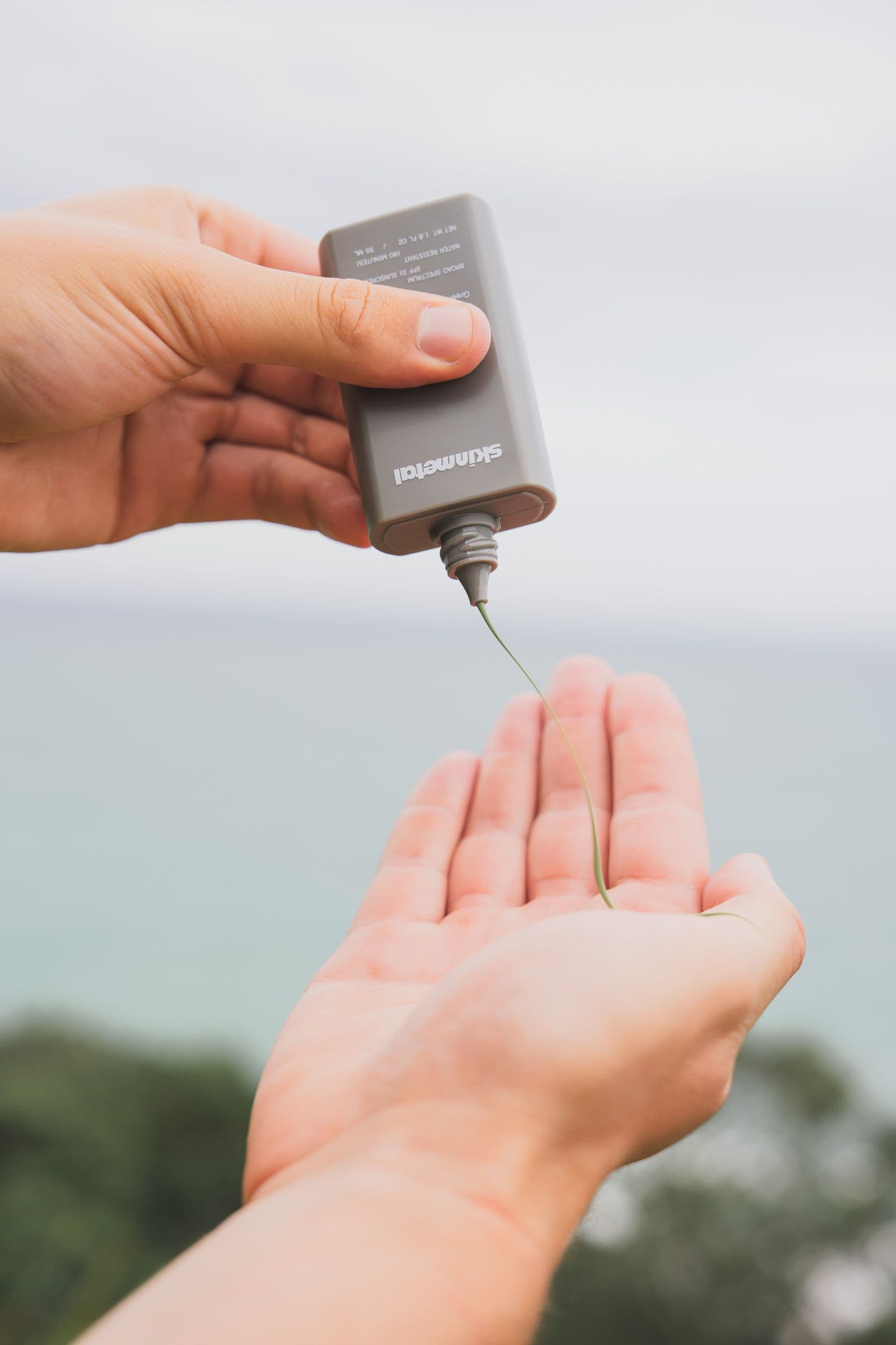 A thin stream of green sunscreen pours from a Skinmetal bottle into an open palm.