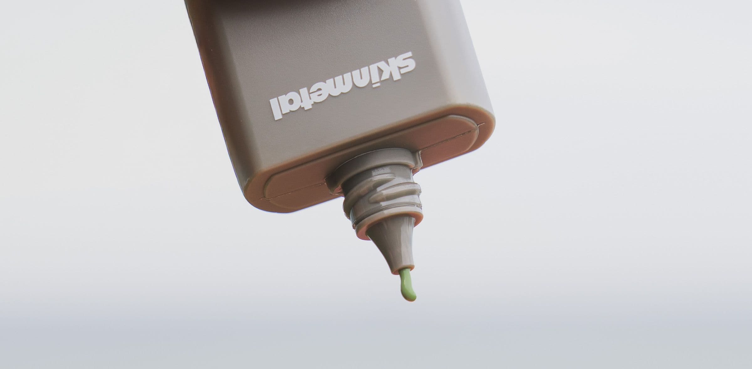 Close-up of a Skinmetal bottle nozzle releasing a green drop of sunscreen.