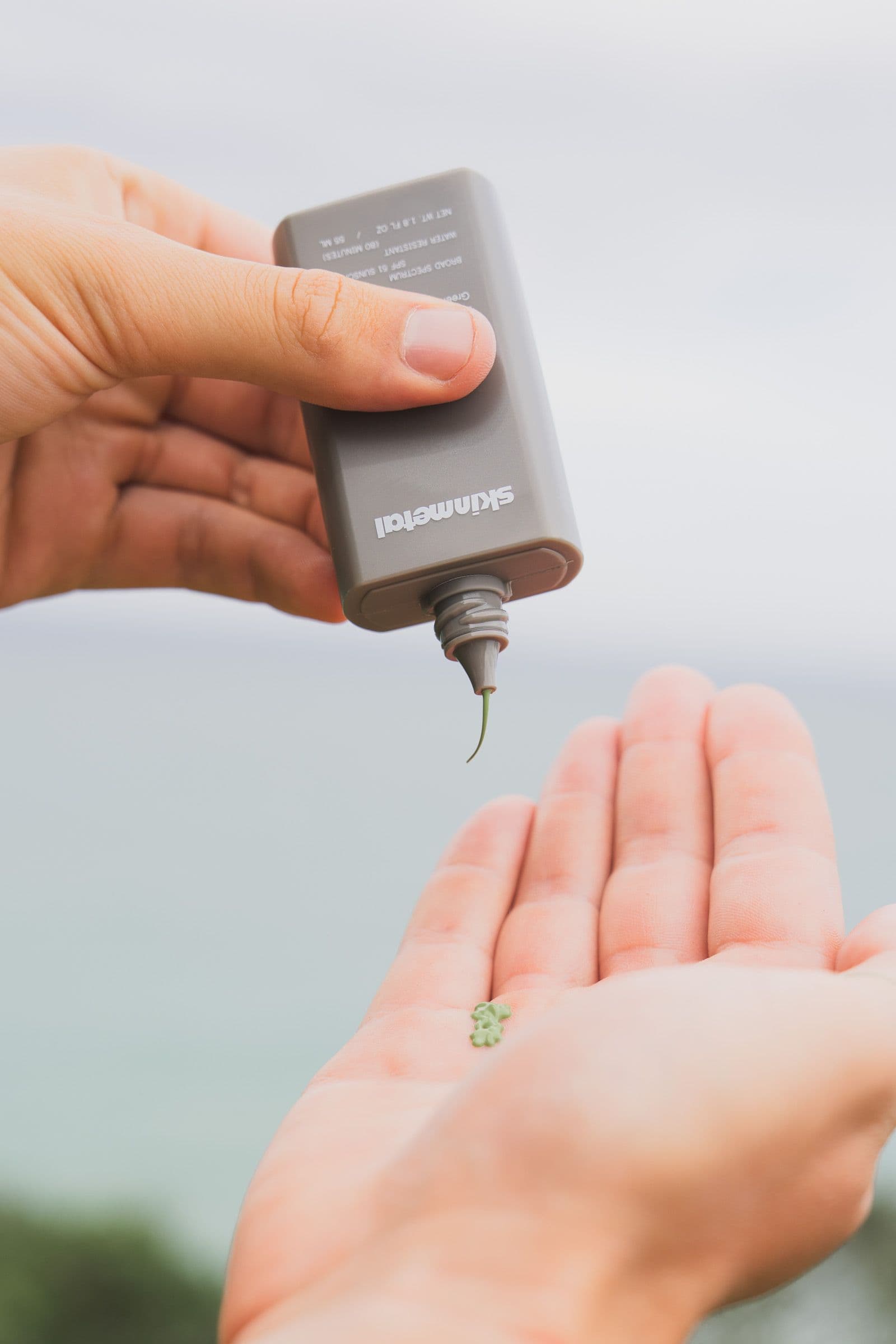 Skinmetal bottle held above an open hand showing a small green dollop of sunscreen.