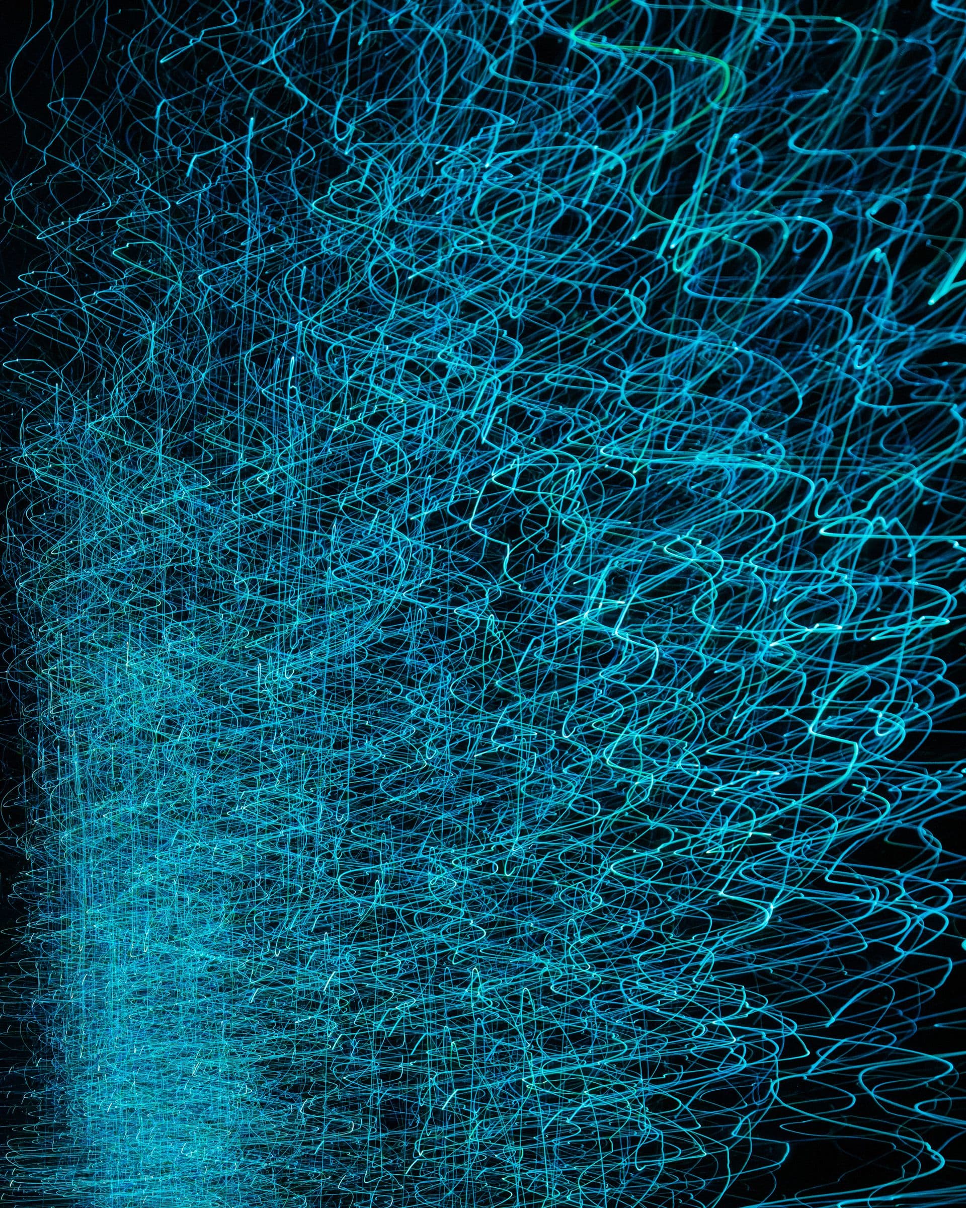 Abstract long exposure of glowing blue light trails swirling against a dark background.